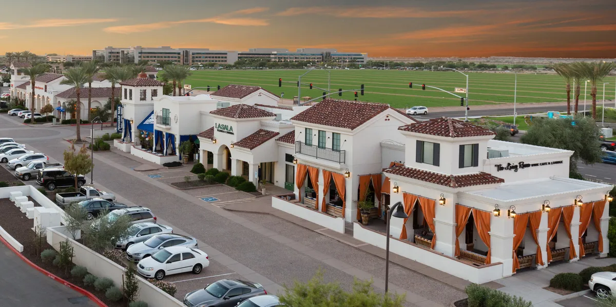 A vibrant, bustling outdoor area with colorful draped curtains, distinctive building architecture, and palm trees, suggesting al fresco dining, socializing, and walkable access to nearby eateries or coffee shops.