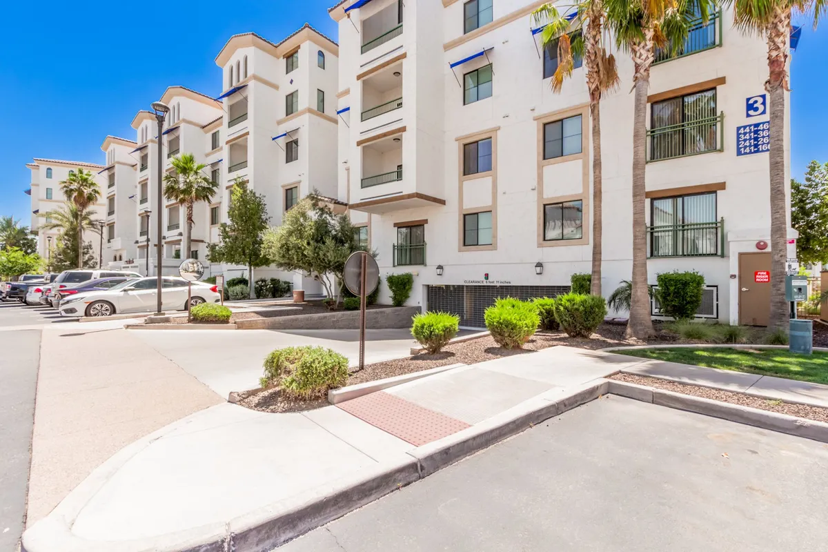 This exterior image showcases modern architectural lines, palm trees, landscaped greenery, and a clearly visible parking area. The scene conveys a feeling of tranquility and convenience in a well-maintained resort community.