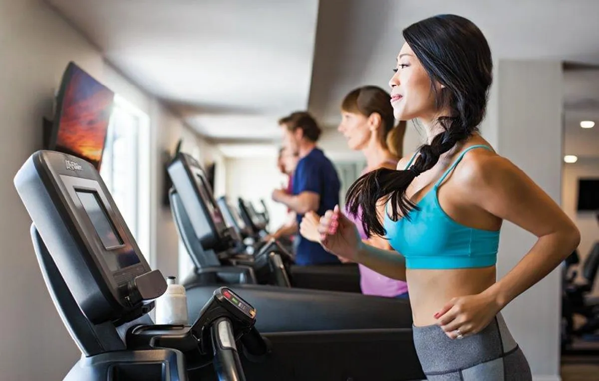 A modern fitness center featuring treadmills, active runners, and a television screen displaying workout content. The bright, energetic space is designed for motivation and achievement, catering to residents who value health and wellness as part of their daily routine.