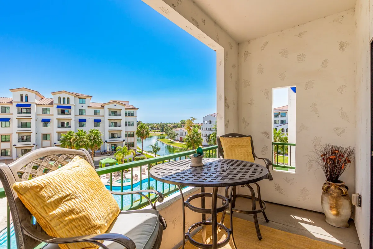 A stylish exterior balcony setup, featuring comfortable furniture overlooking a sparkling pool and landscaped grounds. The scene captures morning light filtering through the trees, hinting at the relaxing, approachable lifestyle available just steps away from the condo.
