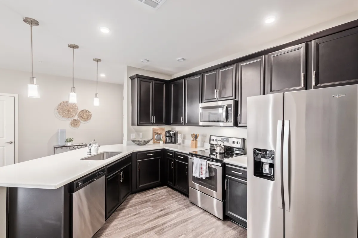A modern kitchen featuring a central island with quartz-look countertops, stainless steel appliances, and dark custom cabinetry. The space exudes a sleek, functional atmosphere perfect for both everyday cooking and social gatherings.