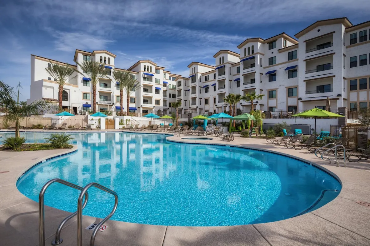 A vibrant exterior scene showcasing a sparkling swimming pool surrounded by lounge chairs and palm trees. Modern buildings frame the background, reinforcing a resort-like atmosphere. The inviting setup is ideal for both daytime relaxation and evening social gatherings, emphasizing leisure and community.