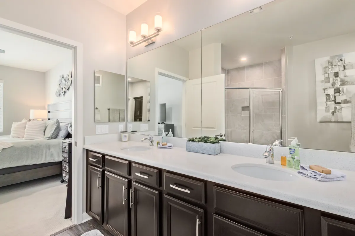 A spa-inspired bathroom with a double sink vanity, large mirrors, a shower area, and tasteful decorative artwork. The space is bright, organized, and designed for relaxation and self-care routines.